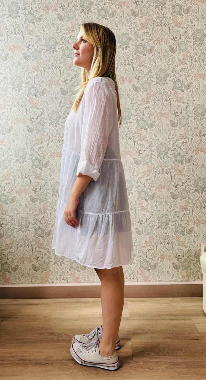 Abito bianco, 100% cotone, scollo a V con manica lunga con risvolto non cucito. Taglio svasato con balze leggere. Perfetto come copricostume. 