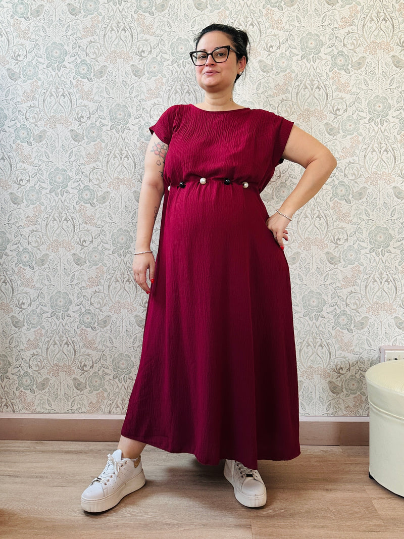 Abito lungo bordeaux con scollo tondo e manica corta. Cintura a nastro in vita regolabile con applicazioni. Vestibilità morbida e ampia. 