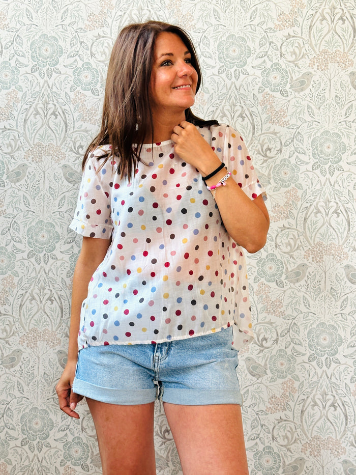 Blusa bianca 100% cotone, con fantasia a pois colorati, svasata sul retro, collo a barchetta. 
