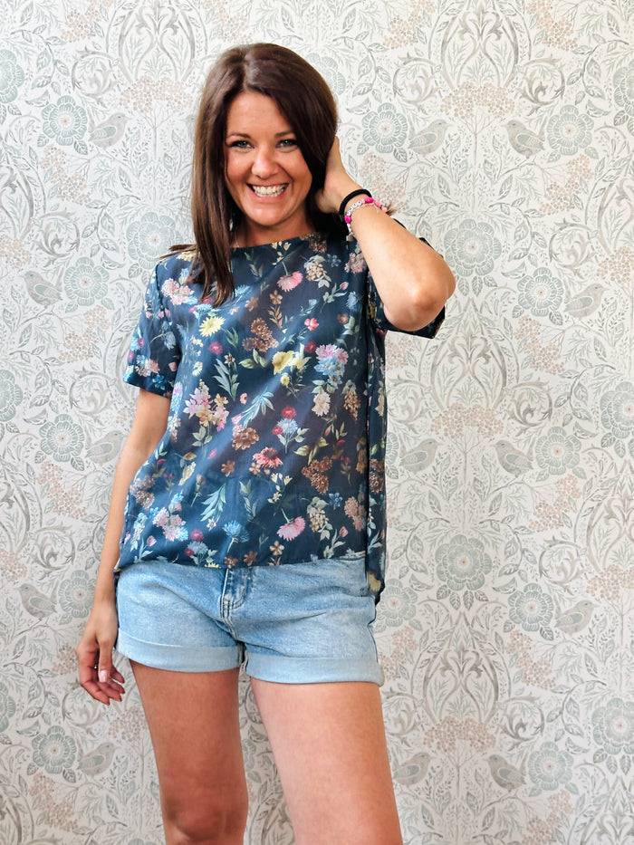 Blusa blu 100% cotone, con fantasia a fiori colorati, svasata sul retro, collo a barchetta. 