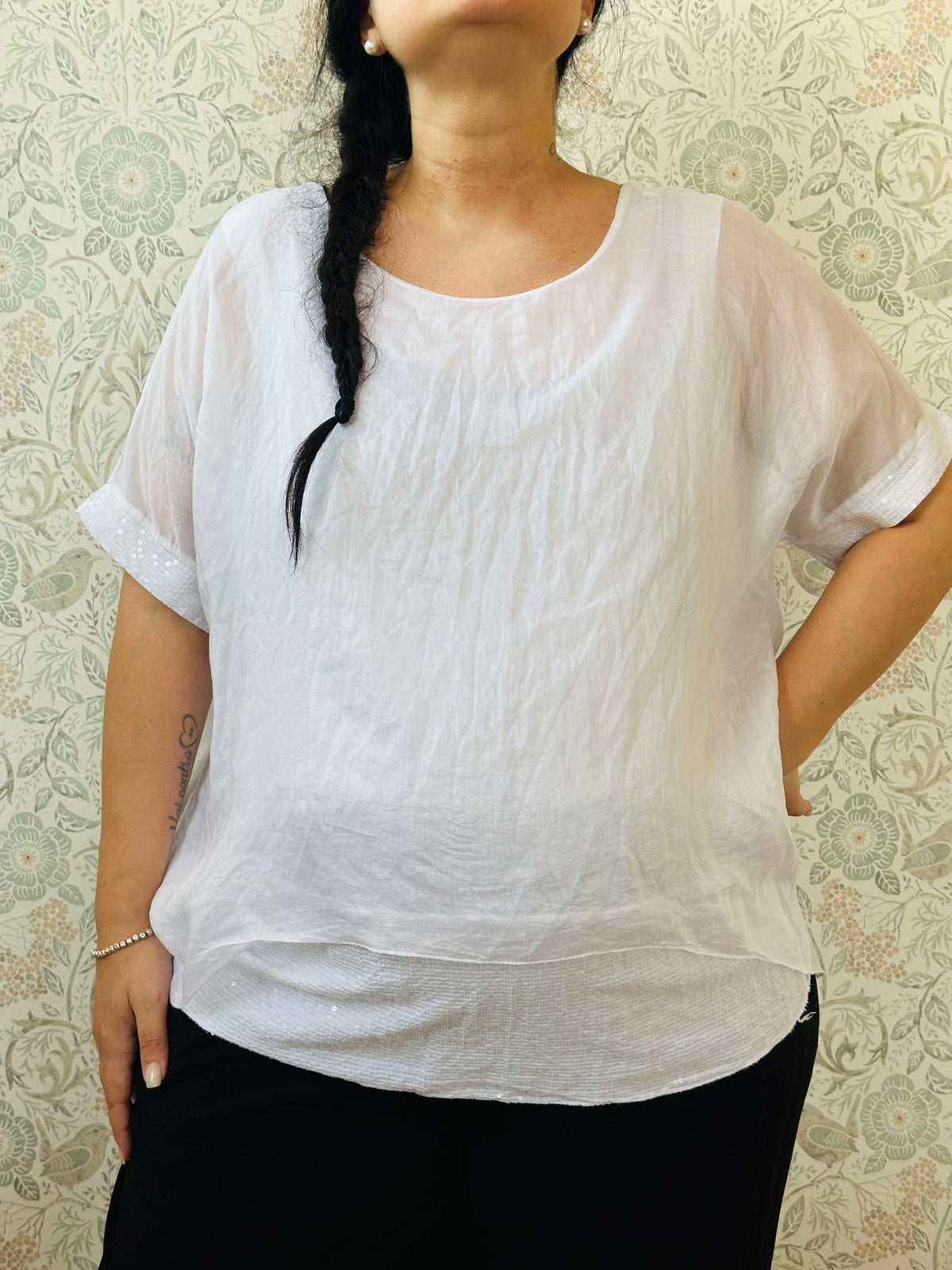 Blusa curvy a manica corta, scollo tondo profondo e top interno in fresca viscosa. Strass applicati sul bordo delle maniche e sul bordo finale del top. 