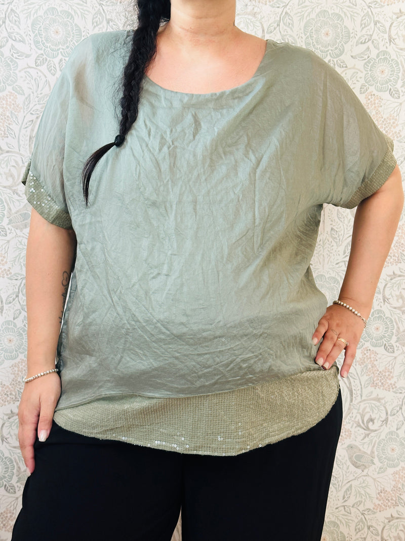Blusa curvy a manica corta, scollo tondo profondo e top interno in fresca viscosa. Strass applicati sul bordo delle maniche e sul bordo finale del top. 