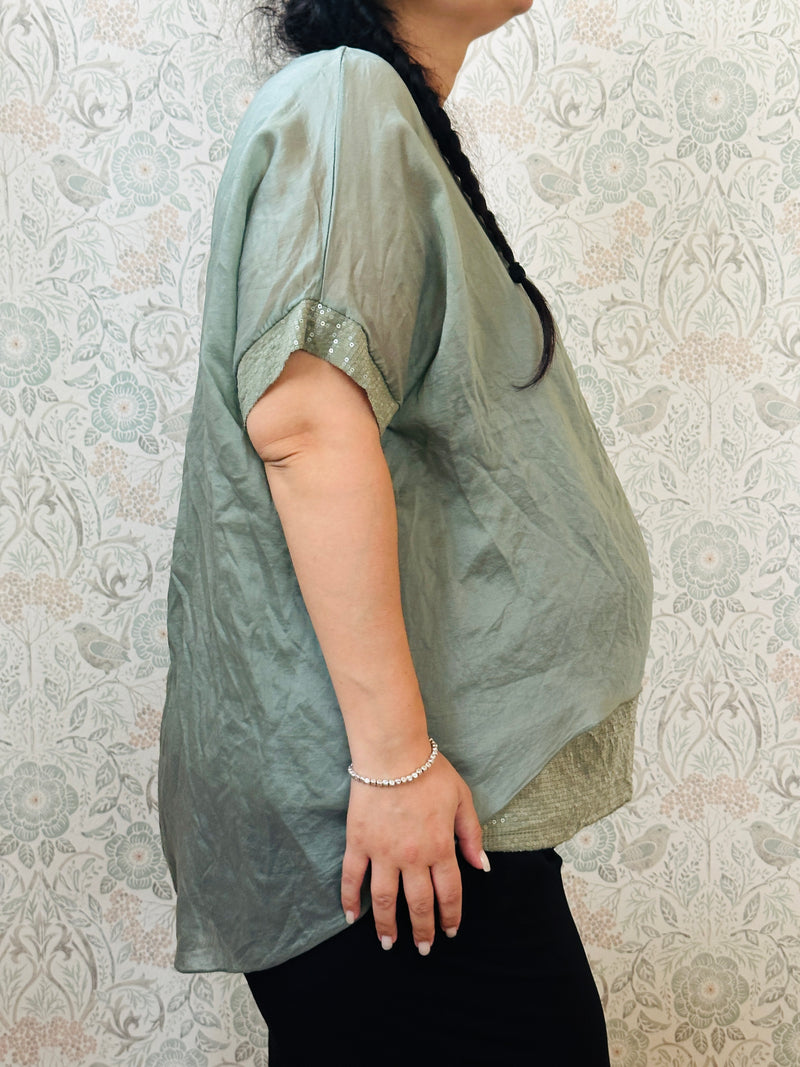 Blusa curvy a manica corta, scollo tondo profondo e top interno in fresca viscosa. Strass applicati sul bordo delle maniche e sul bordo finale del top. 