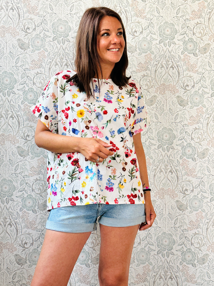 Blusa bianca con fiori colorati, 100% cotone con scollo tondo ampio, manica corta e taglio svasato. Vestibilità morbida.