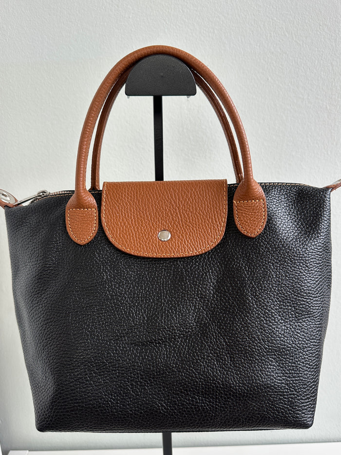 Borsa nera, 100% pelle fiorentina con manici a mano e chiusura con bottone a pressione color cuoio. Chiusura con zip, tasca interna, tracolla regolabile. 