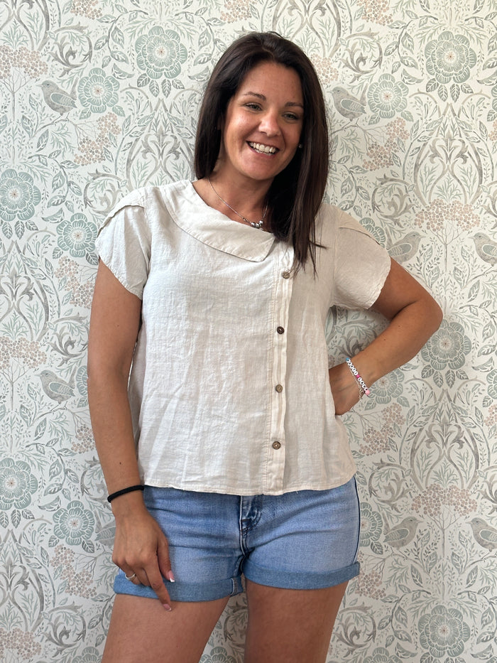Camicia a manica corta con scollo a barchetta, colletto laterale e dettaglio linea con bottoni decorativi. 