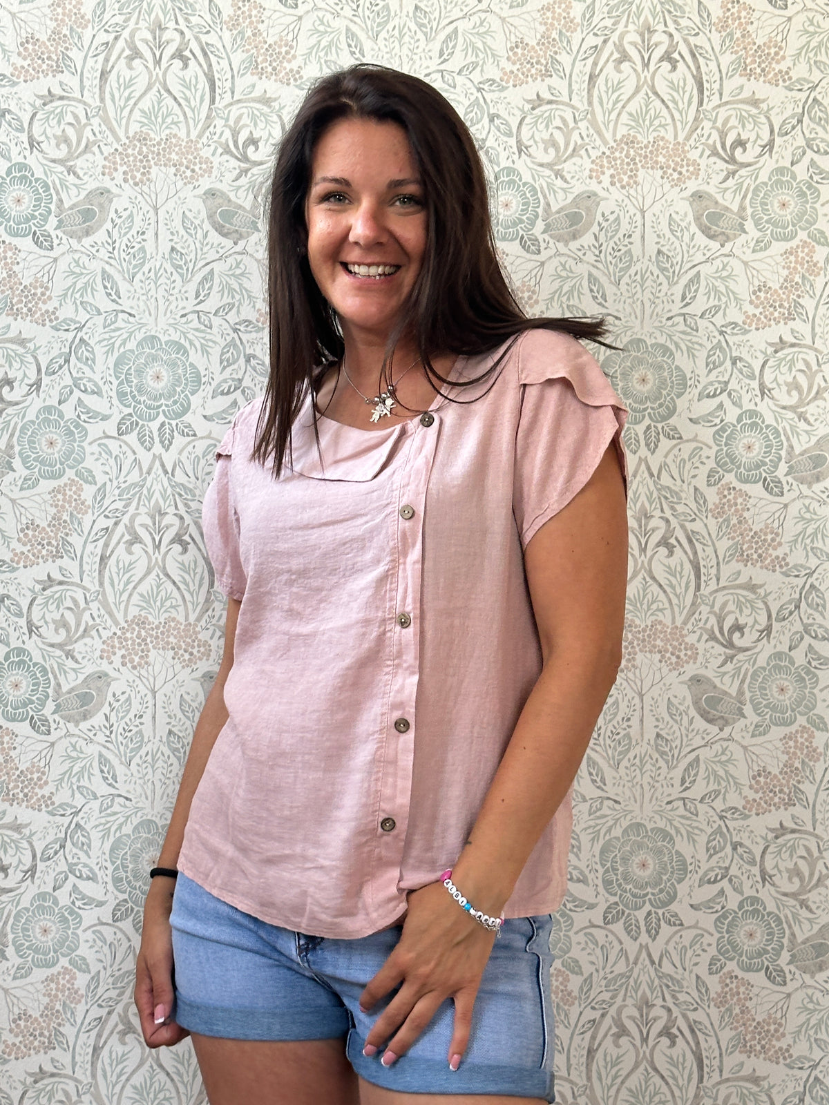 Camicia a manica corta con scollo a barchetta, colletto laterale e dettaglio linea con bottoni decorativi. 