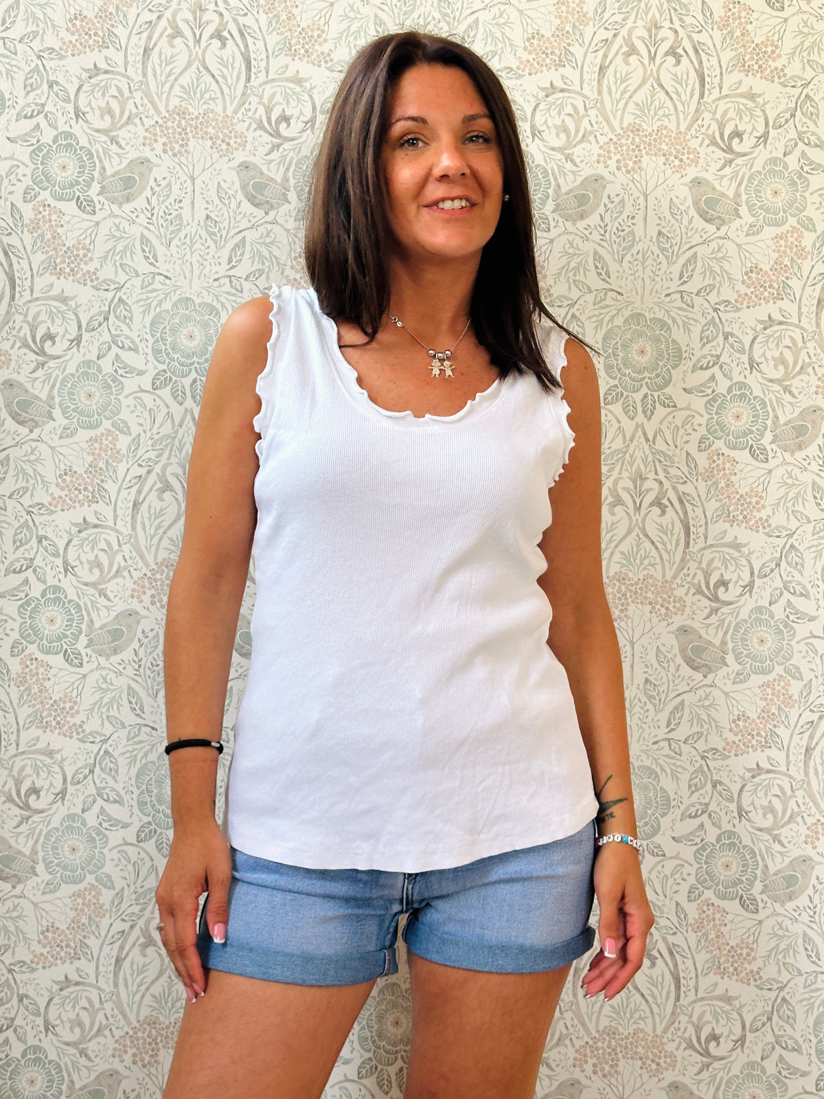 Canotta 100% cotone, scollo tondo con frou frou, tessuto a costine e vestibilità morbida. 