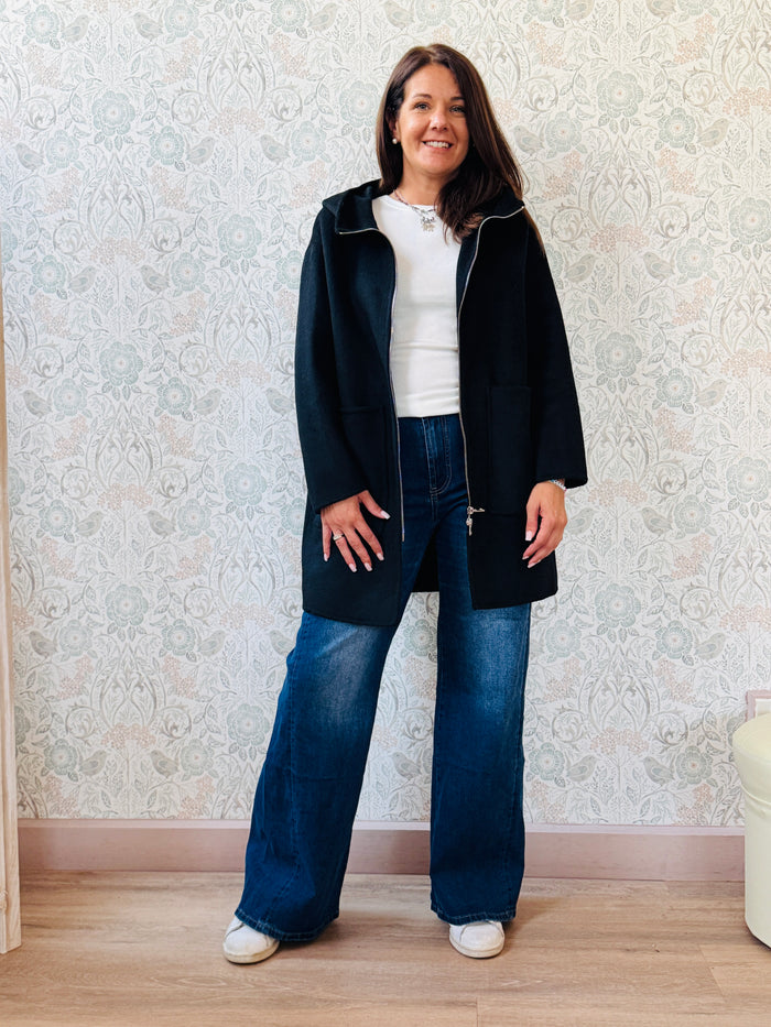 Cappotto nero, taglio dritto e ampio con chiusura zip, cappuccio e tasche sul davanti a viste e aperte. 