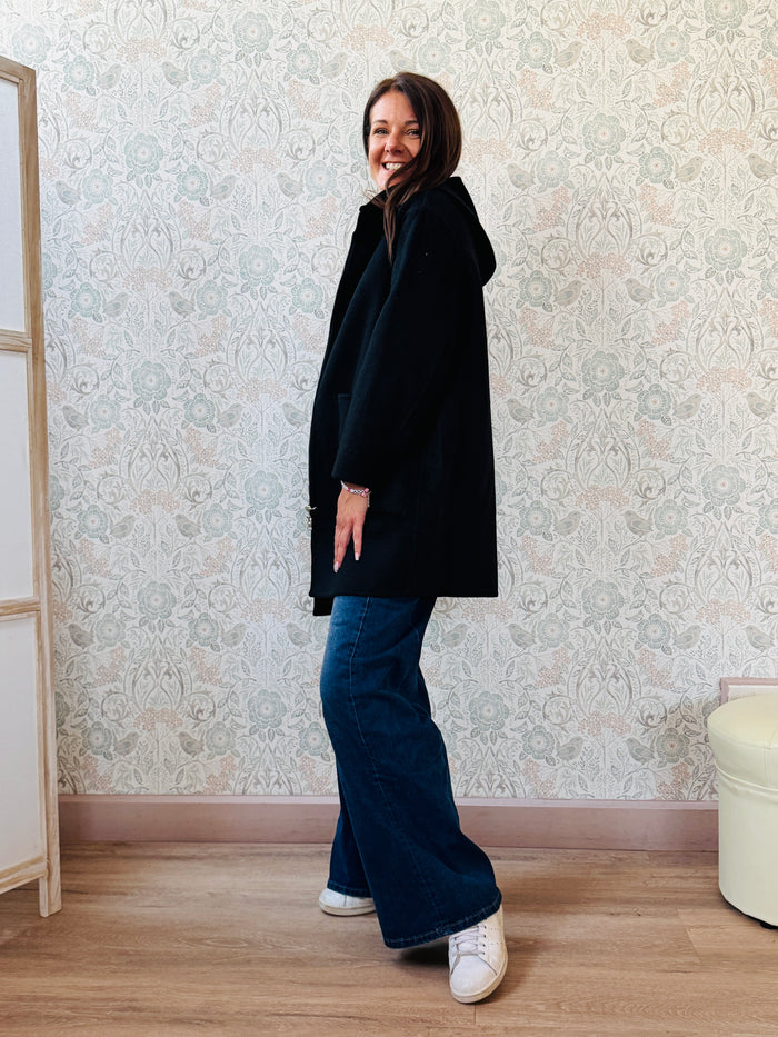 Cappotto nero, taglio dritto e ampio con chiusura zip, cappuccio e tasche sul davanti a viste e aperte. 