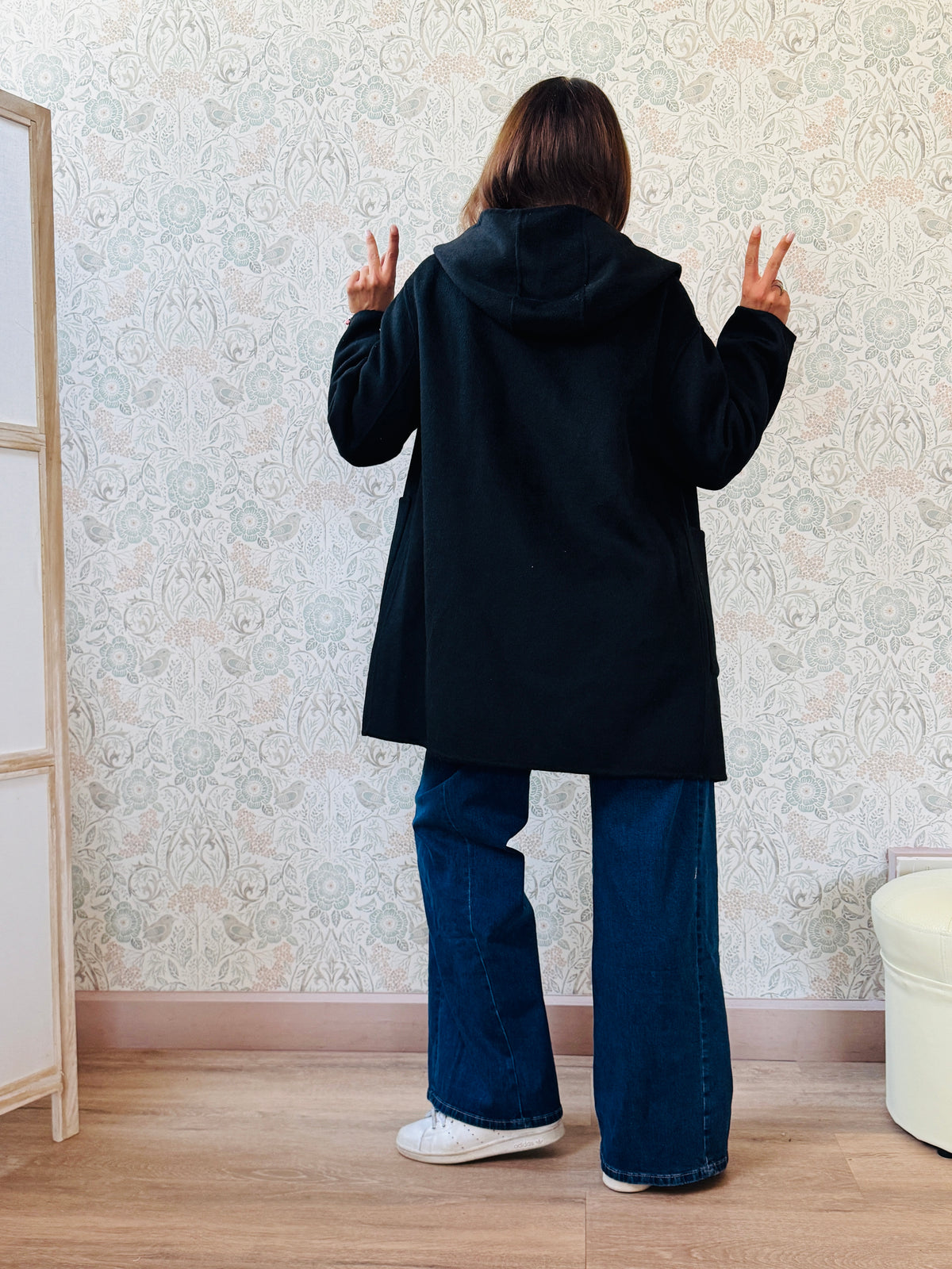 Cappotto nero, taglio dritto e ampio con chiusura zip, cappuccio e tasche sul davanti a viste e aperte. 