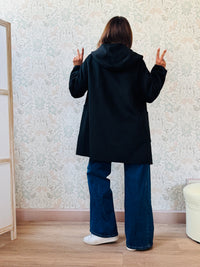 Cappotto nero, taglio dritto e ampio con chiusura zip, cappuccio e tasche sul davanti a viste e aperte. 