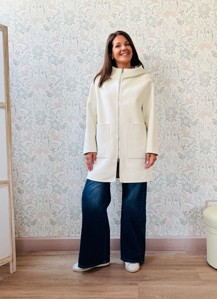 Cappotto color panna, taglio dritto e ampio con chiusura zip, cappuccio e tasche sul davanti a viste e aperte. 