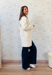 Cappotto color panna, taglio dritto e ampio con chiusura zip, cappuccio e tasche sul davanti a viste e aperte. 