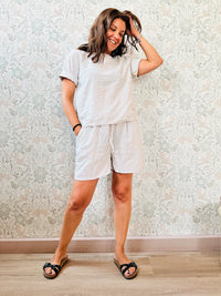 Completo composto da: pantaloncini con elastico in vita, finta coulisse e tasche laterali e blusa svasata a maniche corte con chiusure a bottoni sul retro. 