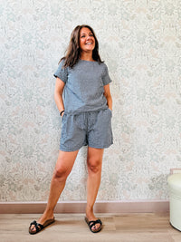 Completo composto da: pantaloncini con elastico in vita, finta coulisse e tasche laterali e blusa svasata a maniche corte con chiusure a bottoni sul retro. 