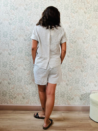 Completo composto da: pantaloncini con elastico in vita, finta coulisse e tasche laterali e blusa svasata a maniche corte con chiusure a bottoni sul retro. 