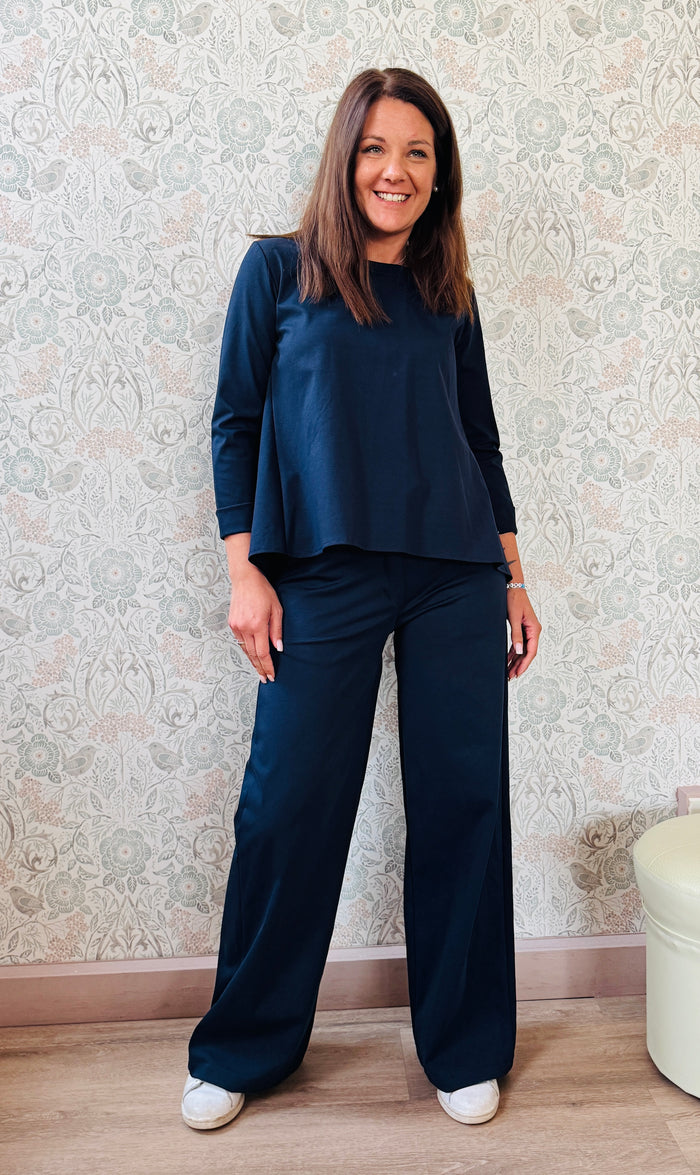 Completo composto da pantaloni con chiusura con zip e cerniera ed elastico sul retro. Taglio a palazzo. Felpa con scollo tondo dal taglio ampio e svasato. 