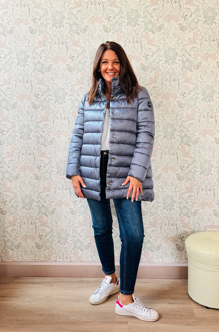 Giubbotto Piumino color blue jeans, lungo con collo alto e chiusura con bottoni a pressione. Tasche laterali con zip.   