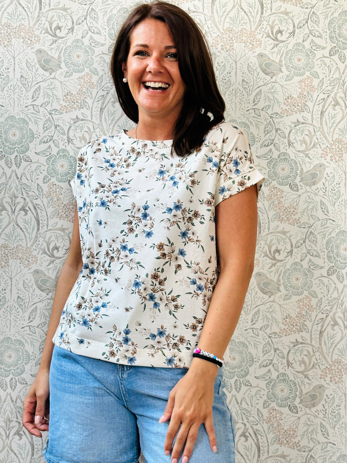 T-shirt con scollo tondo ampio, manica corta leggermente a pipistrello e taglio leggermente svasato. Colore bianco con Fiori azzurri