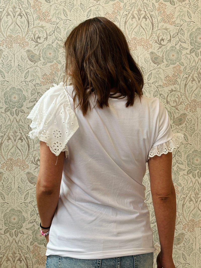 T-shirt bianca a manica corta con dettaglio volant e sangallo. Scollo tondo, taglio dritto e leggermente svasato.