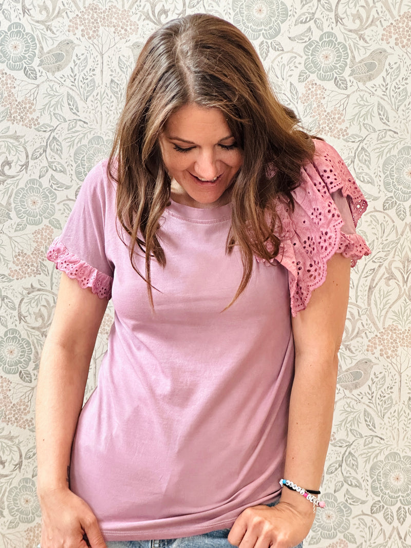 T-shirt rosa a manica corta con dettaglio volant e sangallo. Scollo tondo, taglio dritto e leggermente svasato.