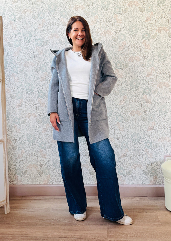 Cappotto grigio taglio dritto e ampio con chiusura zip, cappuccio e tasche sul davanti a viste e aperte. 