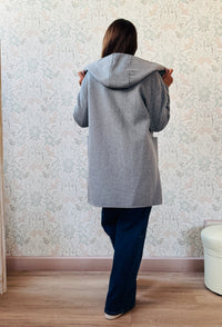 Cappotto grigio taglio dritto e ampio con chiusura zip, cappuccio e tasche sul davanti a viste e aperte. 