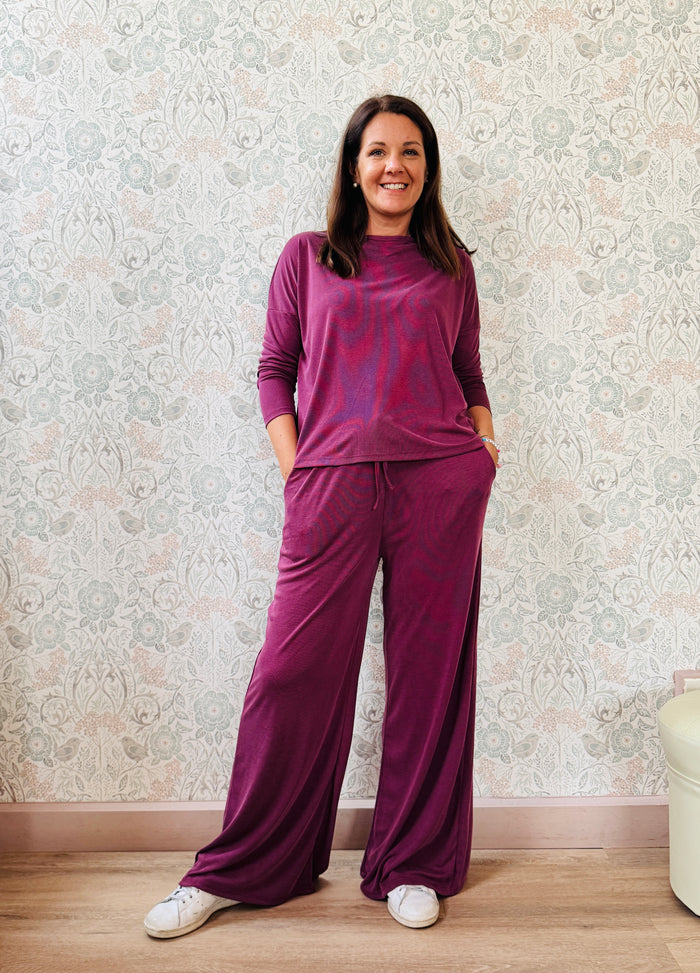 Completo a costine sottili: pantaloni ampi taglio palazzo, elastico in vita, tasche laterali; maglia scollo a barchetta, maniche lunghe e spacchetti laterali 