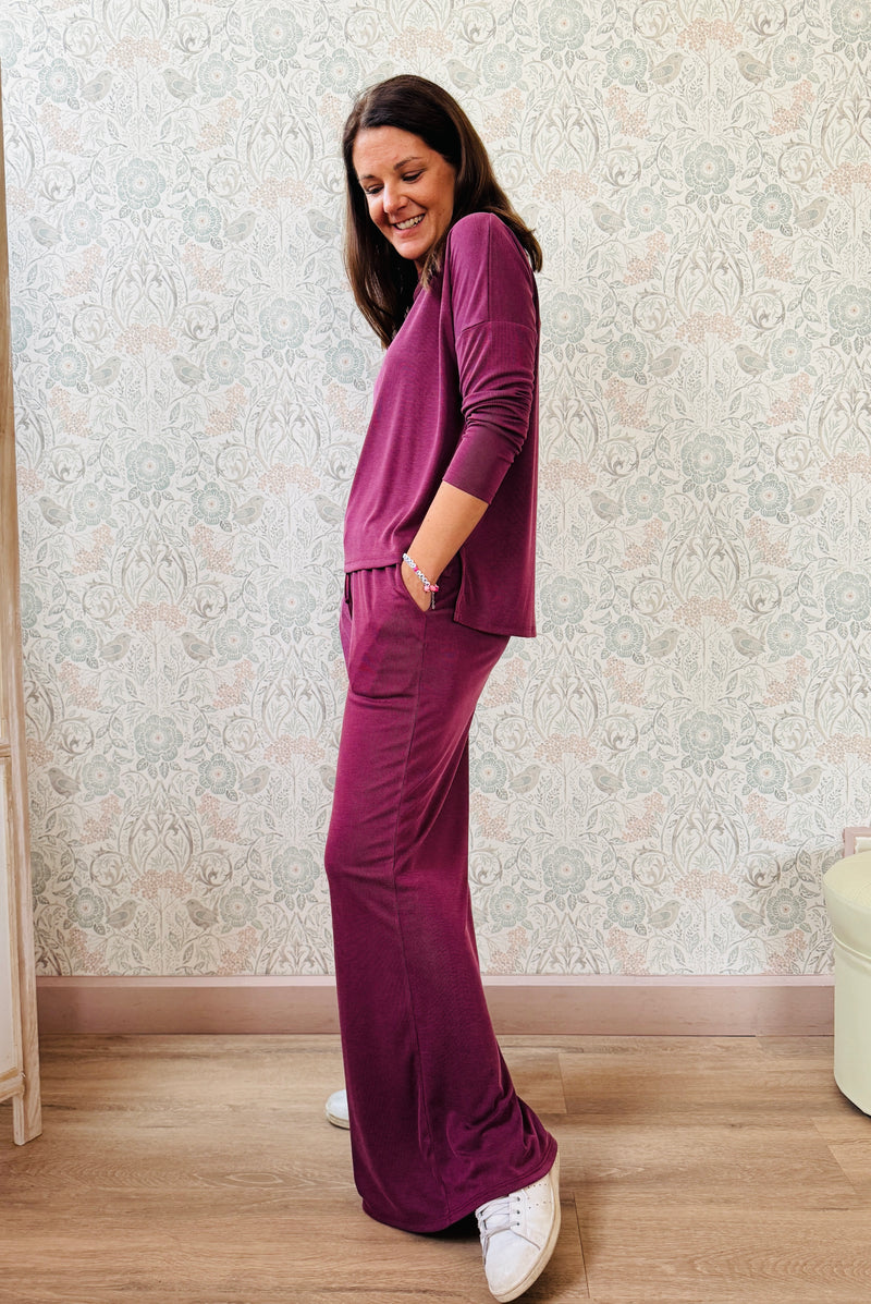Completo a costine sottili: pantaloni ampi taglio palazzo, elastico in vita, tasche laterali; maglia scollo a barchetta, maniche lunghe e spacchetti laterali 