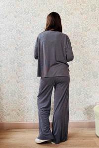 Completo a costine sottili: pantaloni ampi taglio palazzo, elastico in vita, tasche laterali; maglia scollo a barchetta, maniche lunghe e spacchetti laterali 