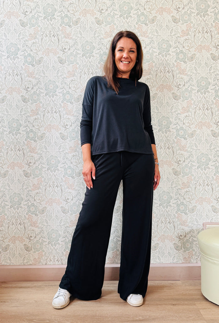Completo a costine sottili: pantaloni taglio palazzo ampio, elastico in vita, tasche laterali; maglia scollo a barchetta, maniche lunghe e spacchetti laterali 