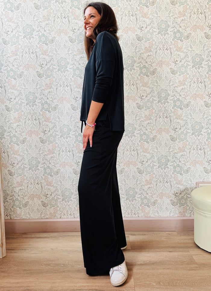 Completo a costine sottili: pantaloni taglio palazzo ampi, elastico in vita, tasche laterali; maglia scollo a barchetta, maniche lunghe e spacchetti laterali 