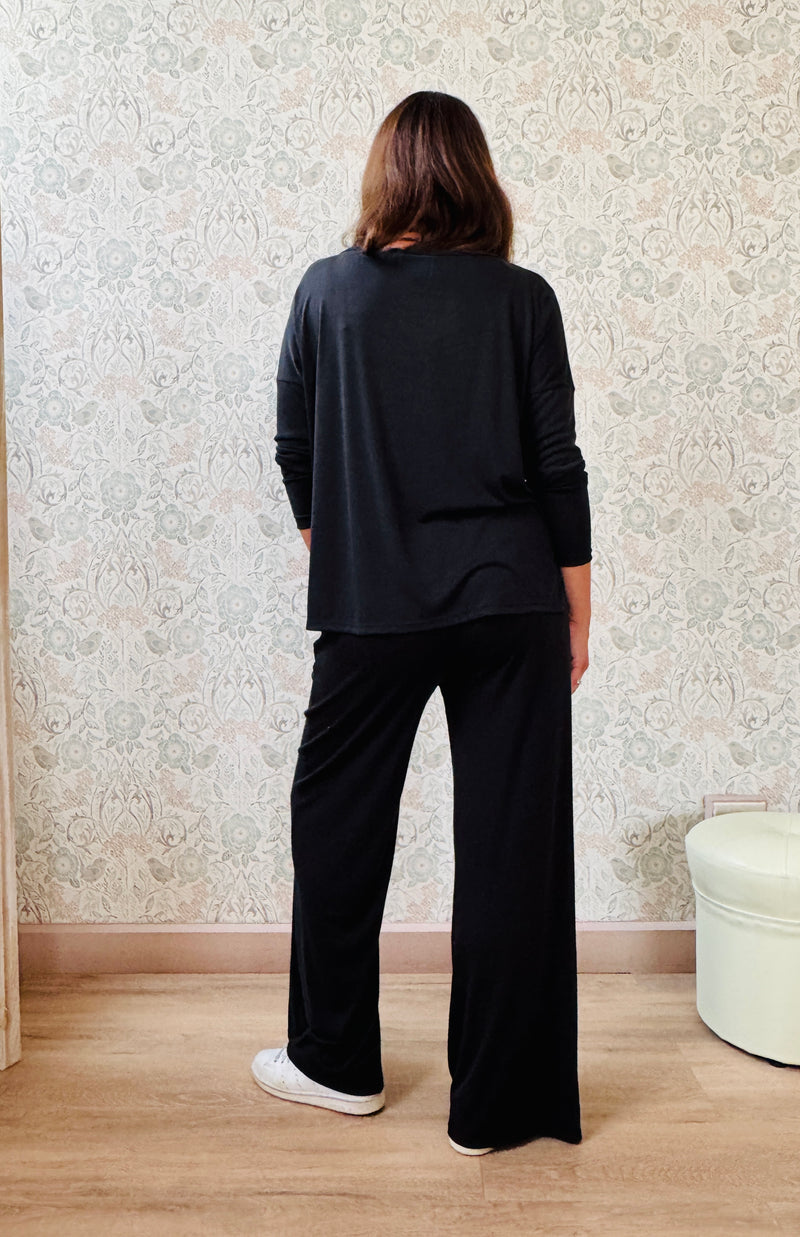 Completo a costine sottili: pantaloni ampi taglio palazzo, elastico in vita, tasche laterali; maglia scollo a barchetta, maniche lunghe e spacchetti laterali 
