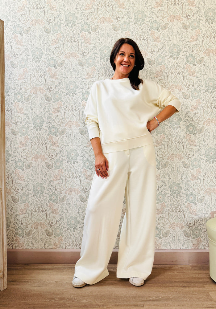 Completo da donna composto da pantaloni ampi con elastico in vita sul retro e tasche laterali; felpa con scollo tondo, manica lunga e spacchetti laterali. 