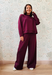 Completo da donna composto da pantaloni ampi con elastico in vita sul retro e tasche laterali; felpa con scollo tondo, manica lunga e spacchetti laterali.  