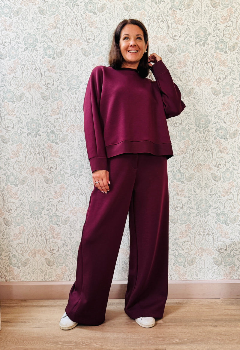 Completo da donna composto da pantaloni ampi con elastico in vita sul retro e tasche laterali; felpa con scollo tondo, manica lunga e spacchetti laterali.  
