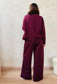 Completo da donna composto da pantaloni ampi con elastico in vita sul retro e tasche laterali; felpa con scollo tondo, manica lunga e spacchetti laterali. 