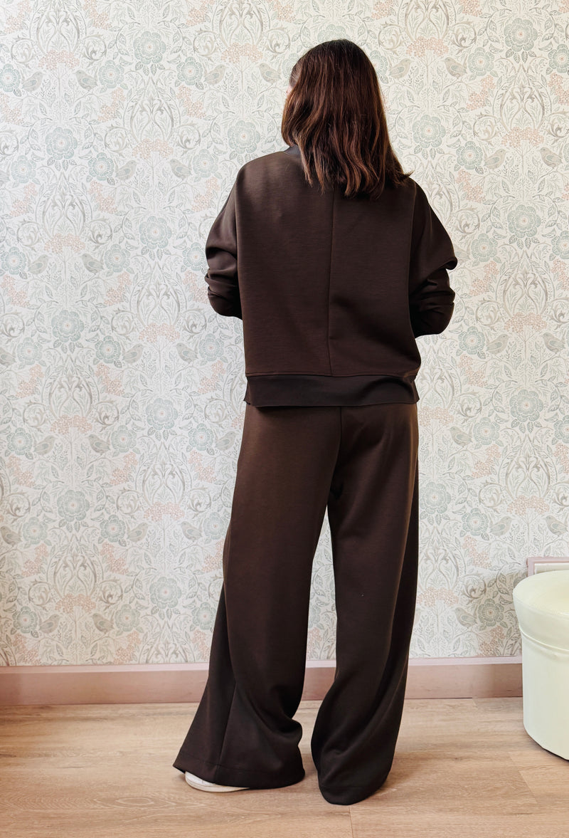 Completo da donna composto da pantaloni ampi con elastico in vita sul retro e tasche laterali; felpa con scollo tondo, manica lunga e spacchetti laterali.  