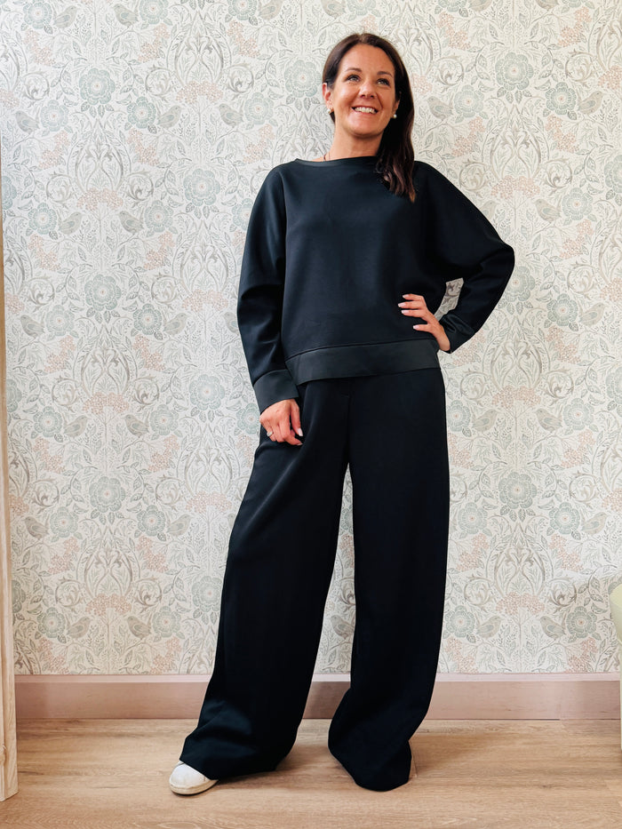 Completo da donna composto da pantaloni ampi con elastico in vita sul retro e tasche laterali; felpa con scollo tondo, manica lunga e spacchetti laterali. 