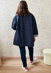 Trench con colletto, chiusura con bottoni ad asola e tasche a vista da aprire. Taglio svasato e fodera interna vichy. 