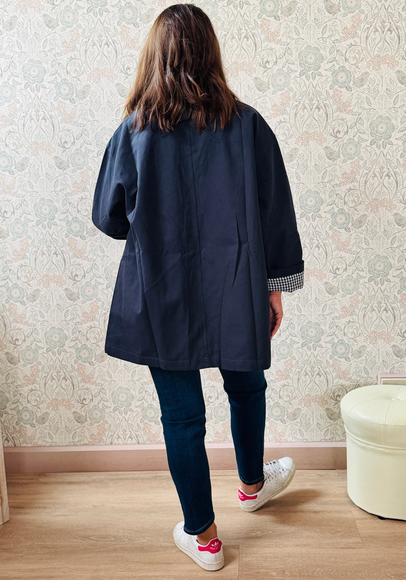 Trench con colletto, chiusura con bottoni ad asola e tasche a vista da aprire. Taglio svasato e fodera interna vichy. 